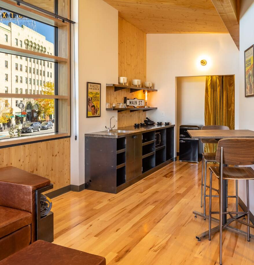 Inside the suite lounge at our downtown Bozeman hotel. Wooden accents, countertop & sink, small wooden desk, with large windows overlooking Main Street.